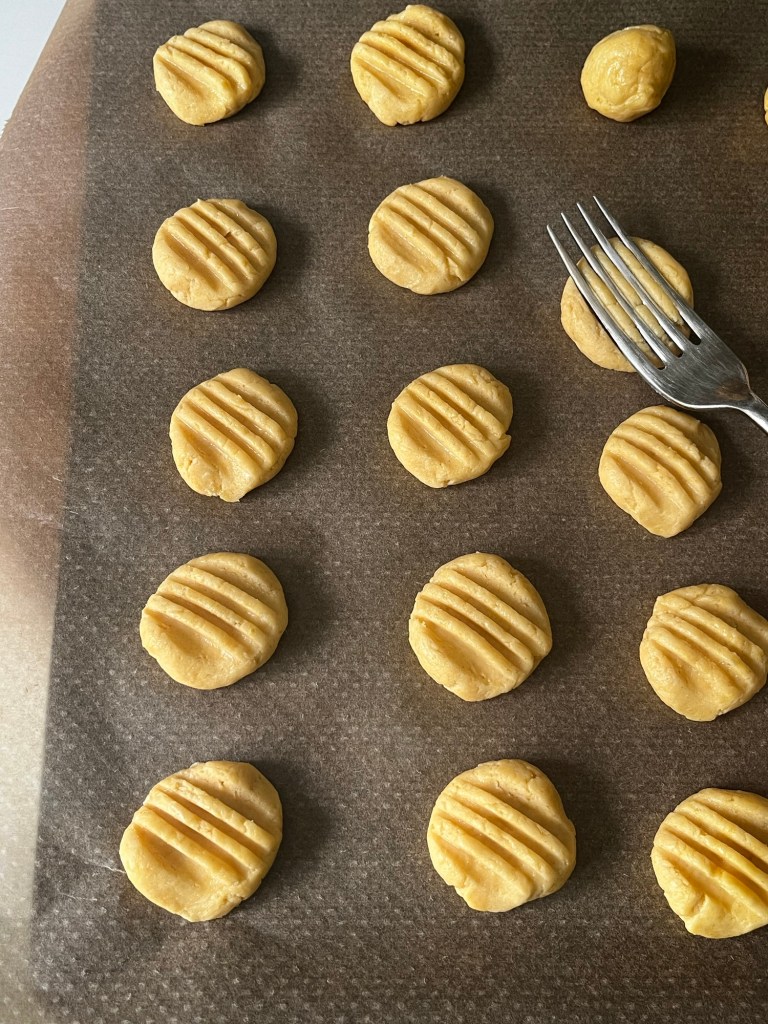 Unbaked cookie dough balls arranged neatly on parchment paper, some with fork markings.