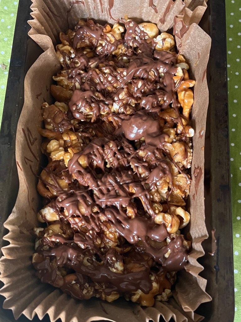 A tray lined with parchment paper filled with a mixture of popcorn, pretzels, and drizzled chocolate.