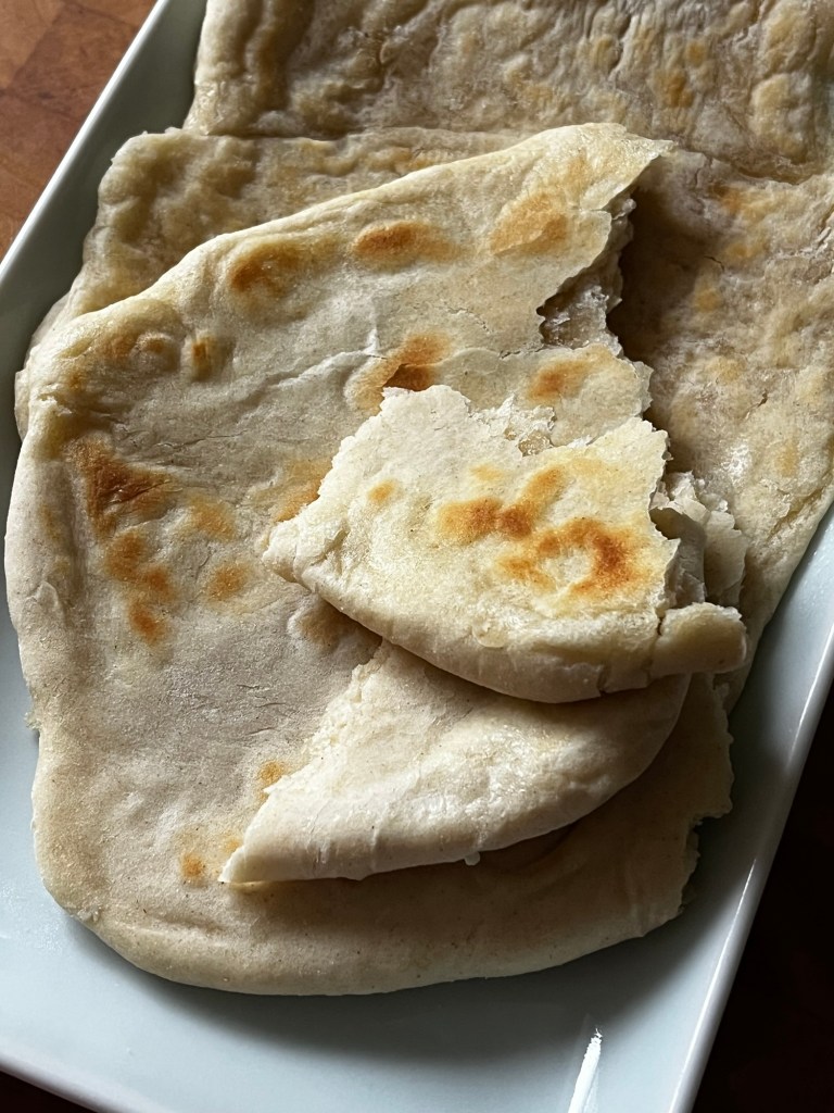 A plate of freshly cooked flatbreads with golden-brown spots, some pieces torn off, showcasing their soft texture.