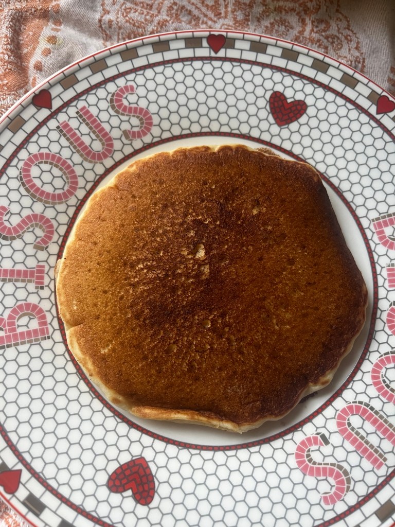 A perfectly cooked pancake on a decorative plate featuring a hexagonal pattern and heart designs.