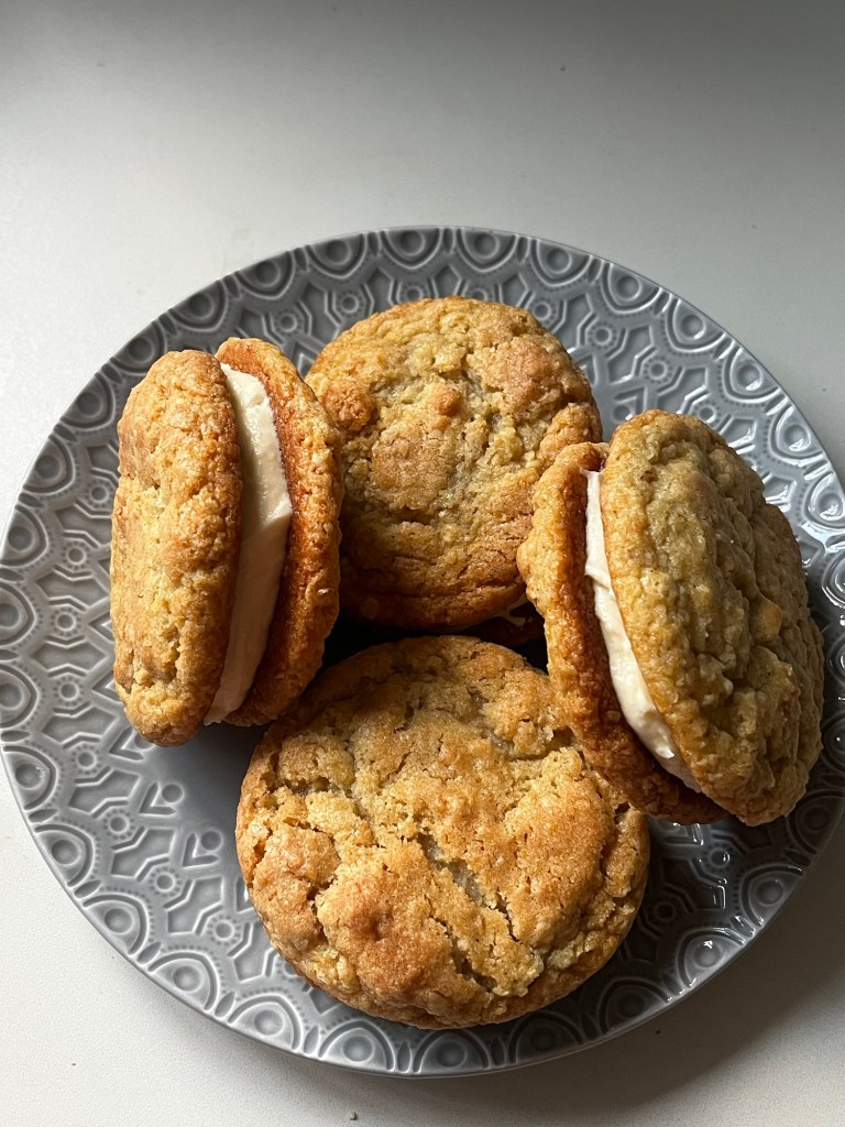 A plate of cookie sandwiches filled with cream, featuring a variety of golden-brown cookies.