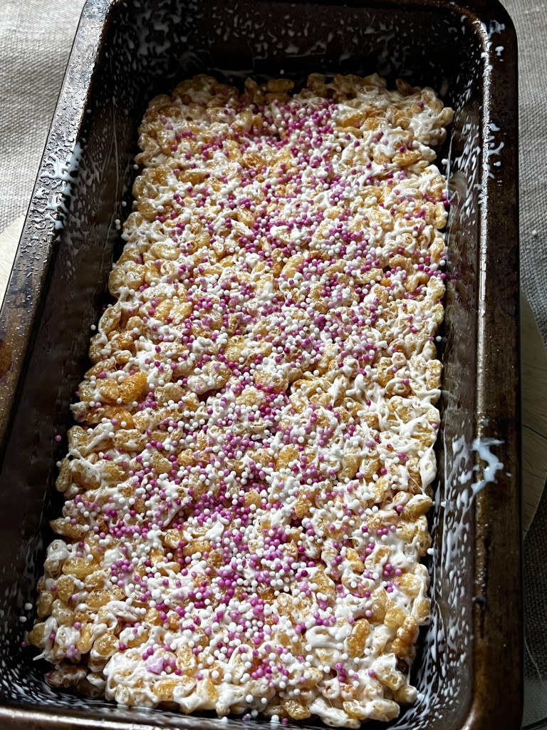 A rectangular tray filled with crispy rice treats topped with white icing and colorful sprinkles.