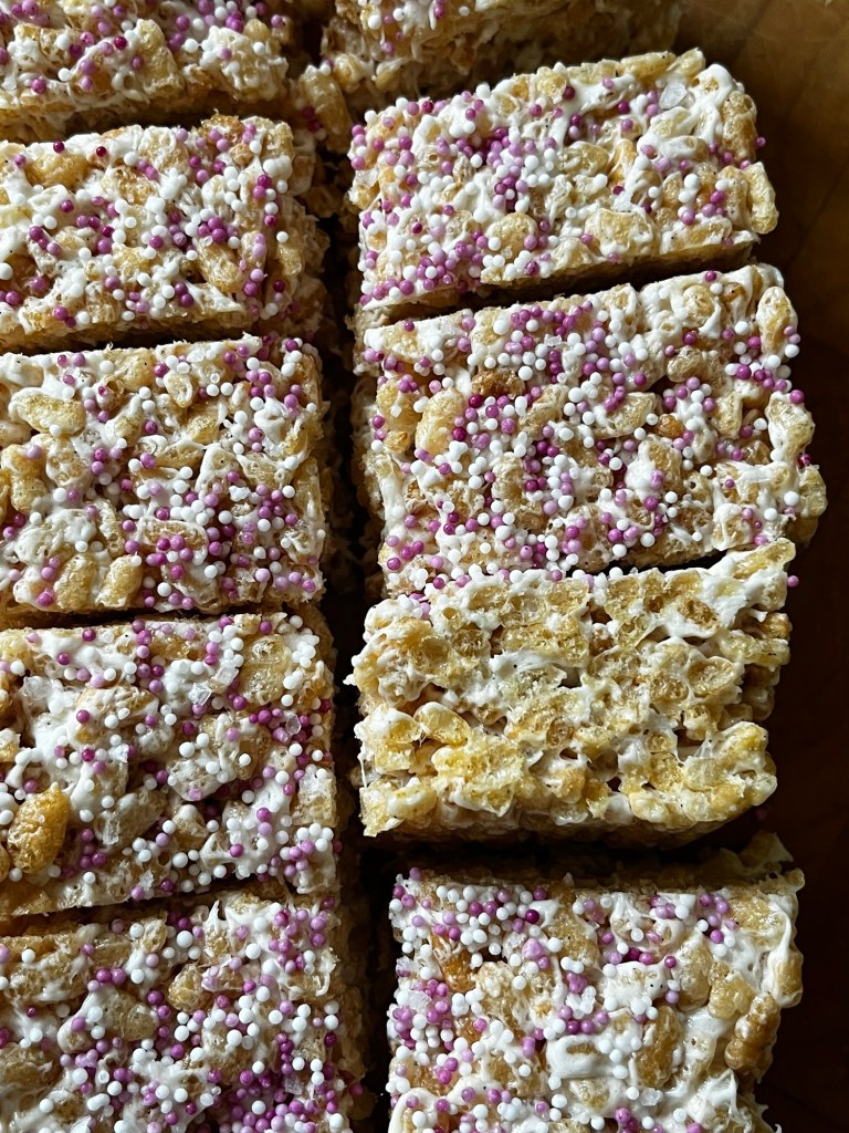 Close-up of cut Rice Krispie treats topped with white icing and colorful sprinkles, arranged neatly in a circular pattern.