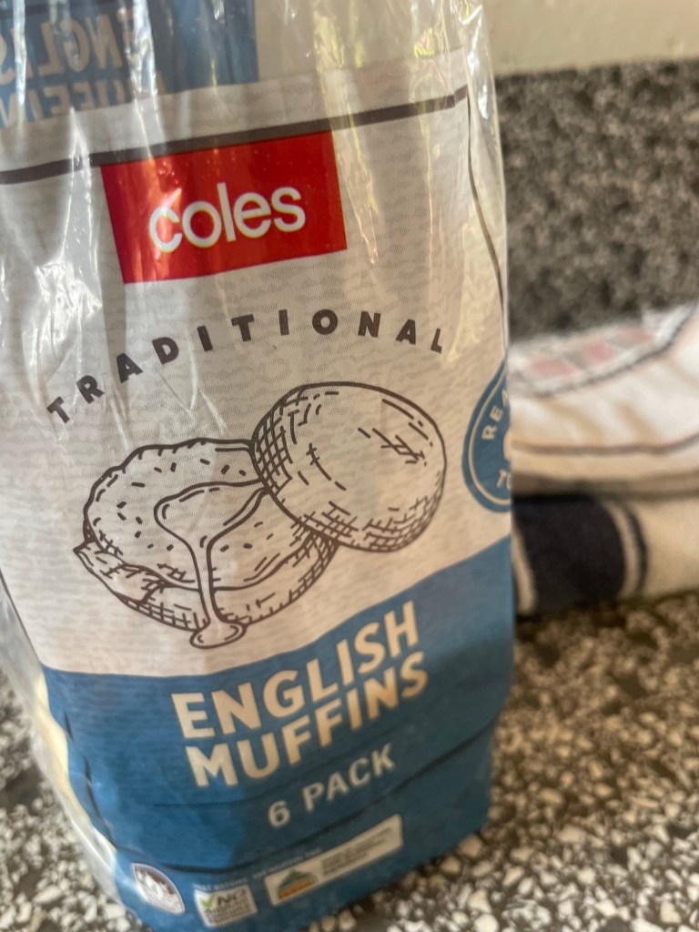 A package of Coles Traditional English Muffins, containing six muffins, displayed on a textured countertop.