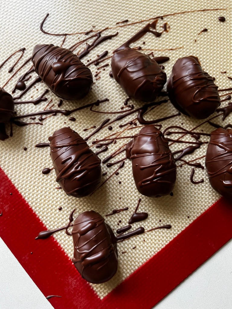 Several chocolate-covered candies arranged on a silicone baking mat, with chocolate drizzles decorating the surface.