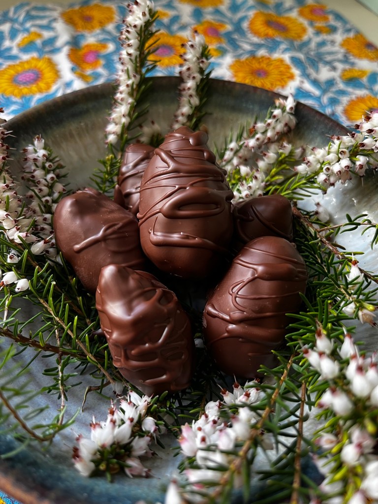 A plate of chocolate-covered eggs decorated with white flowers and greenery, placed on a colorful floral background.
